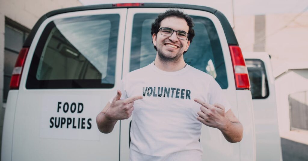 Happy volunteer showing off t-shirt standing in front of a food supplies delivery van outdoors.